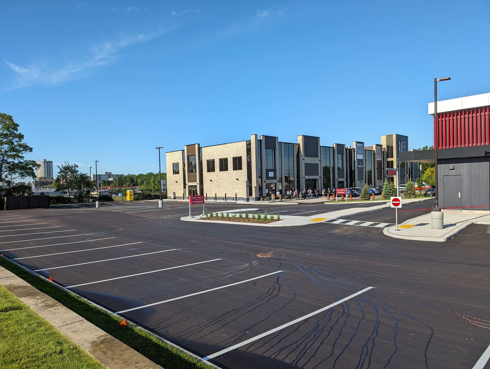 Freshly paved commercial parking lot in front of a retail plaza, featuring crisp white line striping and clean asphalt surface under a clear blue sky in Kitchener, ON.